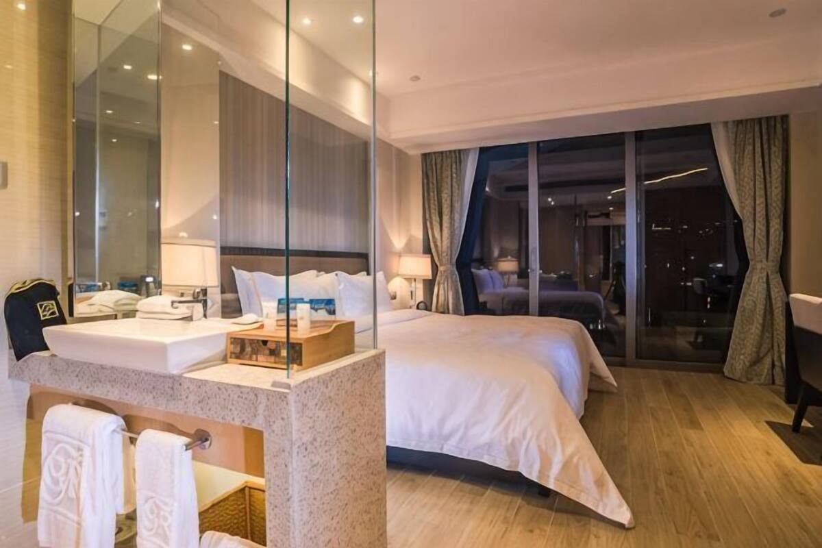 Hotellihuone, jossa on suuri sänky, kylpyhuone peilillä ja näkymä kaupunkiin yöllä.