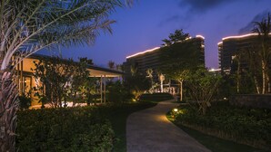 Un chemin bien éclairé mène à un bâtiment moderne doté d’une entrée abritée et entouré d’une végétation luxuriante.