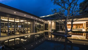 Un bâtiment moderne doté d’un espace repas, d’un bassin d’eau calme et d’un arbre.