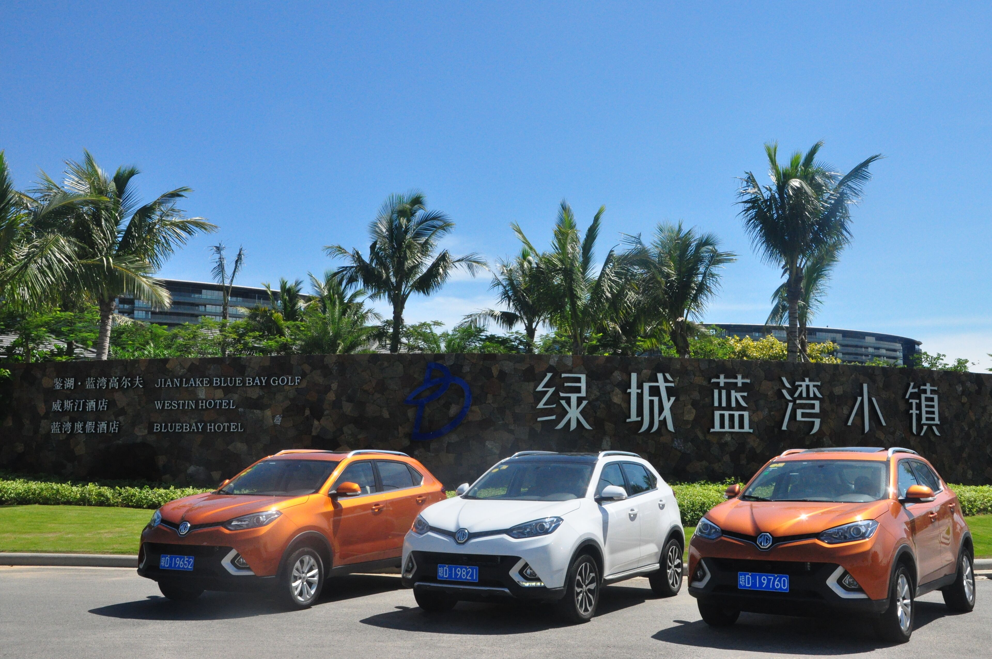 Three cars parked in front of a building with a sign listing nearby hotels and a golf course.