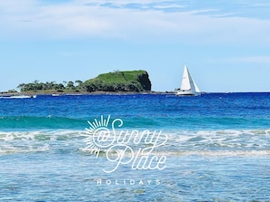 A sailboat on a clear blue sea with a rocky island in the background. - Serene 3BR Beachfront Retreat – Relax & Reconnect (Marcoola)