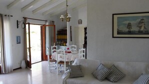 Una sala de estar con sofá, una mesa de comedor con sillas, una araña y un cuadro en la pared.