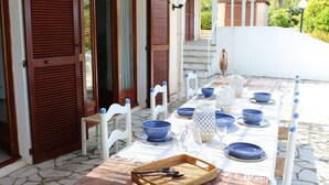 Un área de comedor al aire libre con una mesa preparada para cuatro personas, rodeada de sillas blancas.