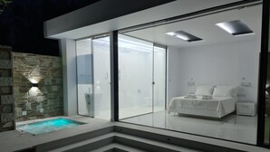 Un dormitorio moderno con puerta de vidrio que da a un balcón, cama empotrada y una mesita de noche pequeña.
