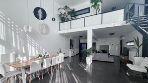 Amplia sala de estar moderna con una mesa de comedor, sillas blancas y una escalera que lleva a un nivel superior.