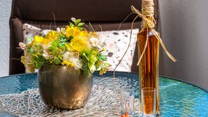 A round glass table with a metal vase of yellow and white flowers, a clear glass bottle with a cork, and a small red flower on the table. - Guest House Kuna (Dubrovnik)