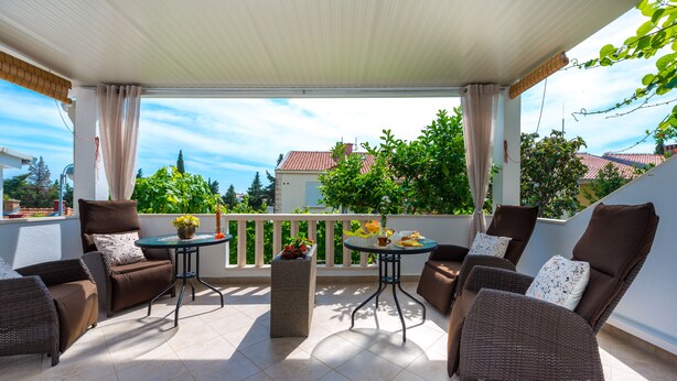 A covered outdoor seating area with wicker furniture, a small table with a vase, and a view of the neighborhood. - Guest House Kuna (Dubrovnik)