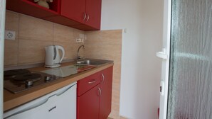 A compact kitchen with a red cabinet, a white countertop, a kettle, and a sink. - Guest House Kuna (Dubrovnik)
