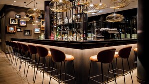 A bar area with a long counter, multiple stools, and hanging light fixtures.