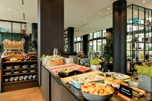 A buffet area with various food items and a sign indicating 'Obstsalat Fruit Salad'. - Motel One Köln-Messe (Cologne)