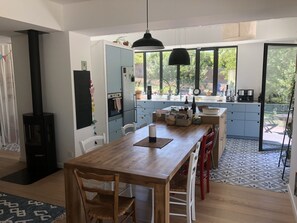 Una cocina moderna con una isla central, un comedor con mesa y sillas de madera, y un amplio ventanal que ofrece vistas al exterior.