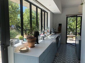 A modern kitchen with large windows, a countertop with potted plants, and a view of the outdoors.