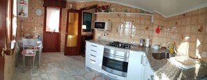 A compact kitchen with a stove, oven, microwave, and a small sink. There is a dining area with a table and chairs.