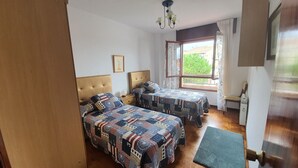 Ein Schlafzimmer mit zwei Betten, einem Holz-Kopfstück, einem Fenster mit Vorhängen und einem kleinen Nachttisch mit Lampe.