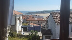 Eine Küstenstadt mit terrakottafarbenen Dächern, ein Strand im Hintergrund und ein klarer Himmel.