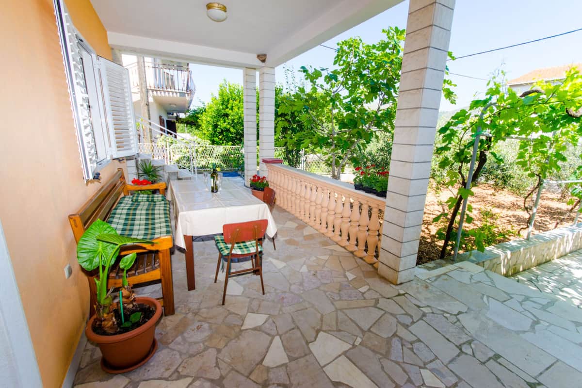 Un espacio de comedor al aire libre con techo, una mesa y sillas, plantas en macetas y vistas al entorno verde.