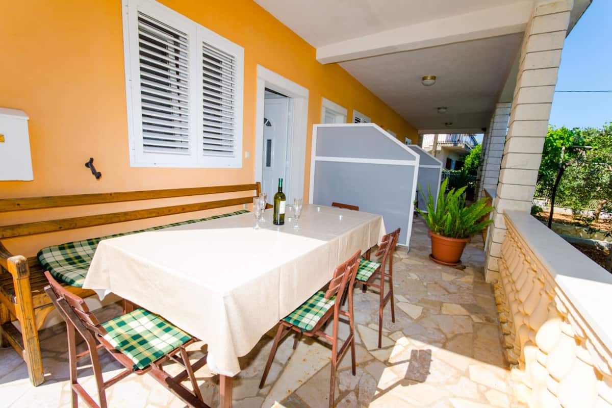 Un área de comedor al aire libre con mesa y sillas, una planta en maceta y una escalera que lleva a un nivel superior.