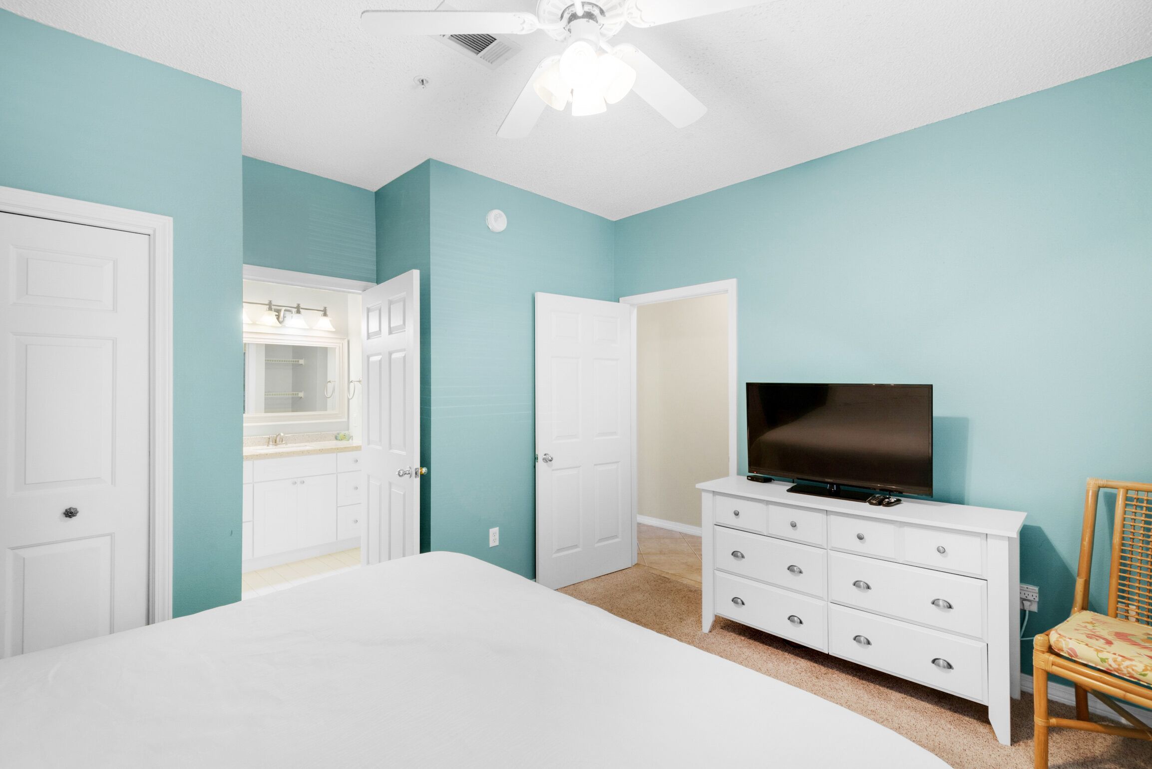 A bedroom with teal walls, white furniture, a bed, a dresser, a television, and a ceiling fan.