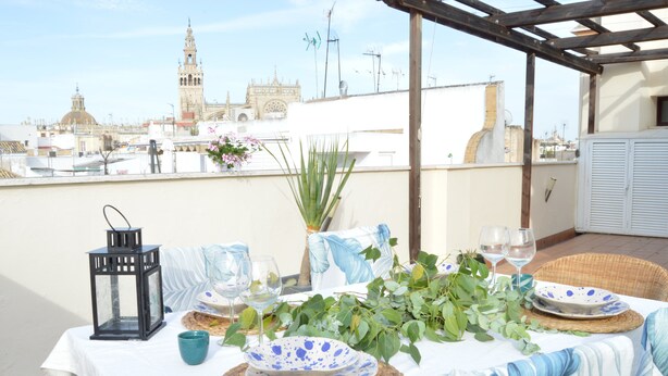 Una terrazza sul tetto con un tavolo apparecchiato per mangiare, con vista su un edificio storico sullo sfondo.