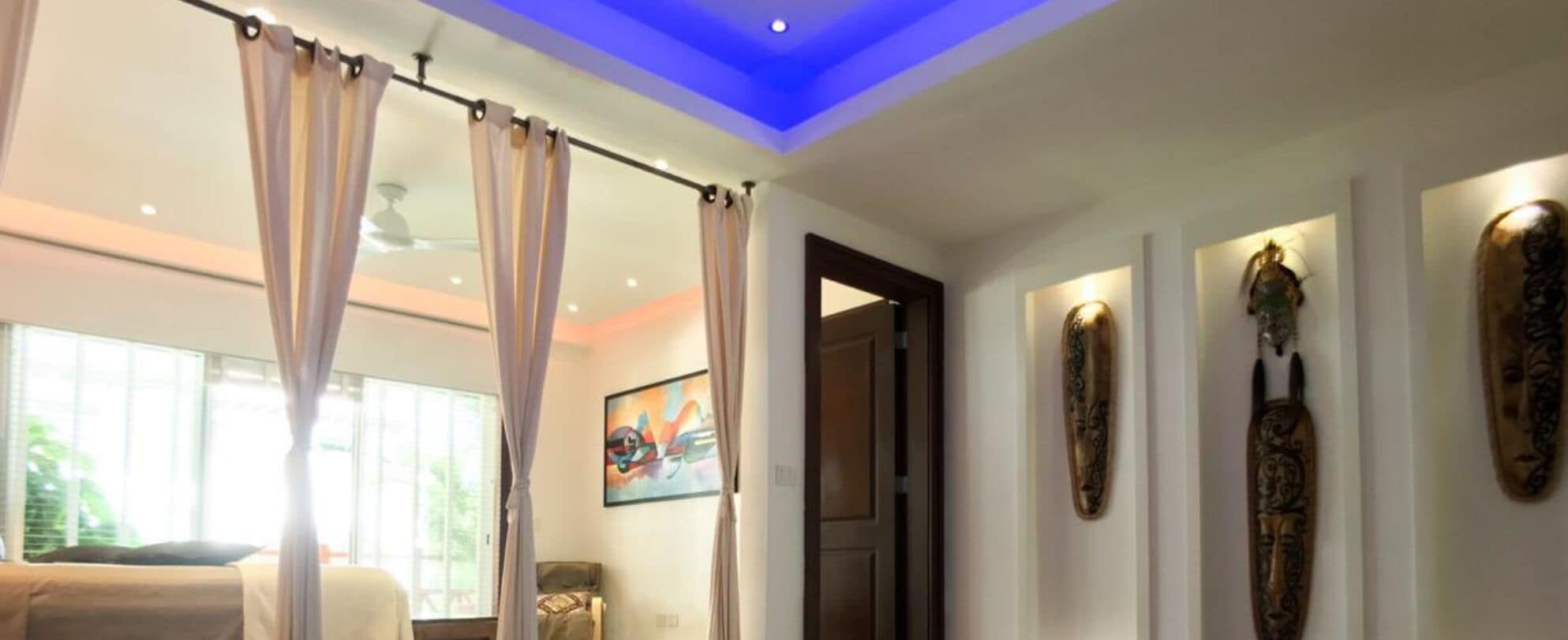 Una habitación con cama, cortinas, una lámpara en el techo y obras de arte colgadas en la pared.