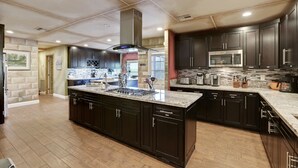 A modern kitchen with dark cabinetry, a large island with a sink, and a stainless steel range hood.