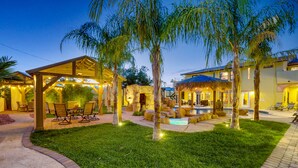 A well-lit outdoor area with a covered seating area, a pool, and a thatched-roof structure.