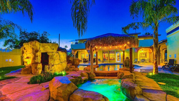 A pool area with a rock formation, a thatched gazebo, and outdoor seating.