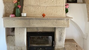 Een stenen open haard met een mantel bovenop, een vaas met bloemen en een klein oranje beeldje.