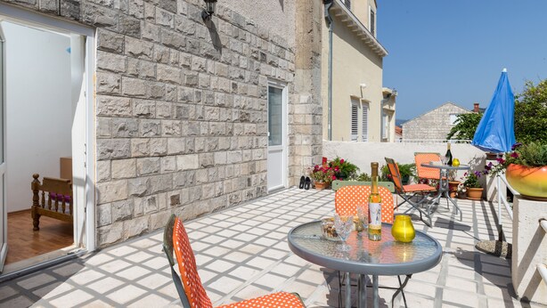 Une terrasse extérieure avec un mur en pierre, une table en verre et des chaises orange.