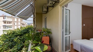 Un balcon avec un auvent à rayures, une chaise, un lit et une porte.