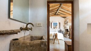 Une salle de bain rustique avec un lavabo en pierre, une porte en bois donnant sur une chambre, et un plafond recouvert de chaume.