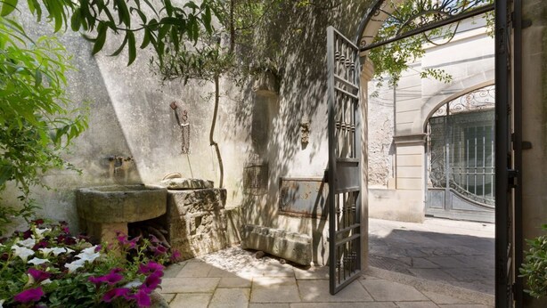 Une cour avec un banc en pierre, une petite fontaine et une porte.