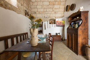 A rustic dining area with a wooden table, benches, a vase with flowers, and a bookshelf. - Characteristic historic home for 4 / Puglia (Sternatia)