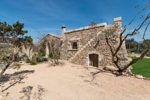 A stone building with a window and a door, surrounded by trees and a grassy area.