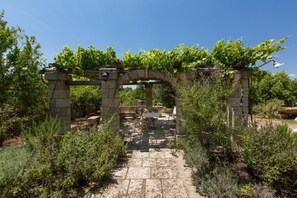 An outdoor stone archway with a table and chairs underneath, surrounded by greenery.