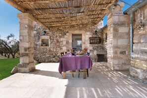 A stone building with a covered patio, a table with a purple tablecloth, and a stone fireplace.