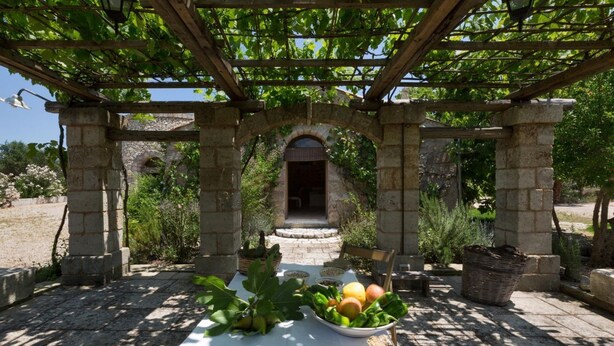 Una pergola in pietra con un tavolo apparecchiato per un pasto, immersa nel verde.