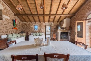 Un intérieur rustique avec des murs en pierre, un plafond en bois, une table à manger avec des chaises, une cheminée et un coin salon confortable.