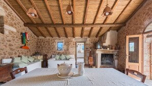 Un interno rustico in pietra con soffitto in legno, un tavolo da pranzo con sedie, un camino e un'accogliente zona salotto.