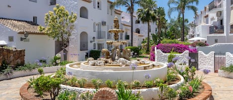 A courtyard with a central fountain, surrounded by white buildings with balconies and arched windows.