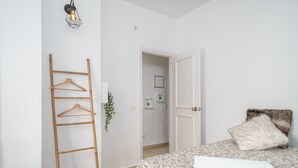 Un dormitori amb un llit, una escala de fusta, una planta penjant i una porta que dona a una altra habitació.