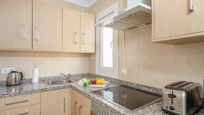 Cuina amb armaris de fusta, taulell de granat, forn de sobretaula, torradora i finestra que deixa entrar llum natural.