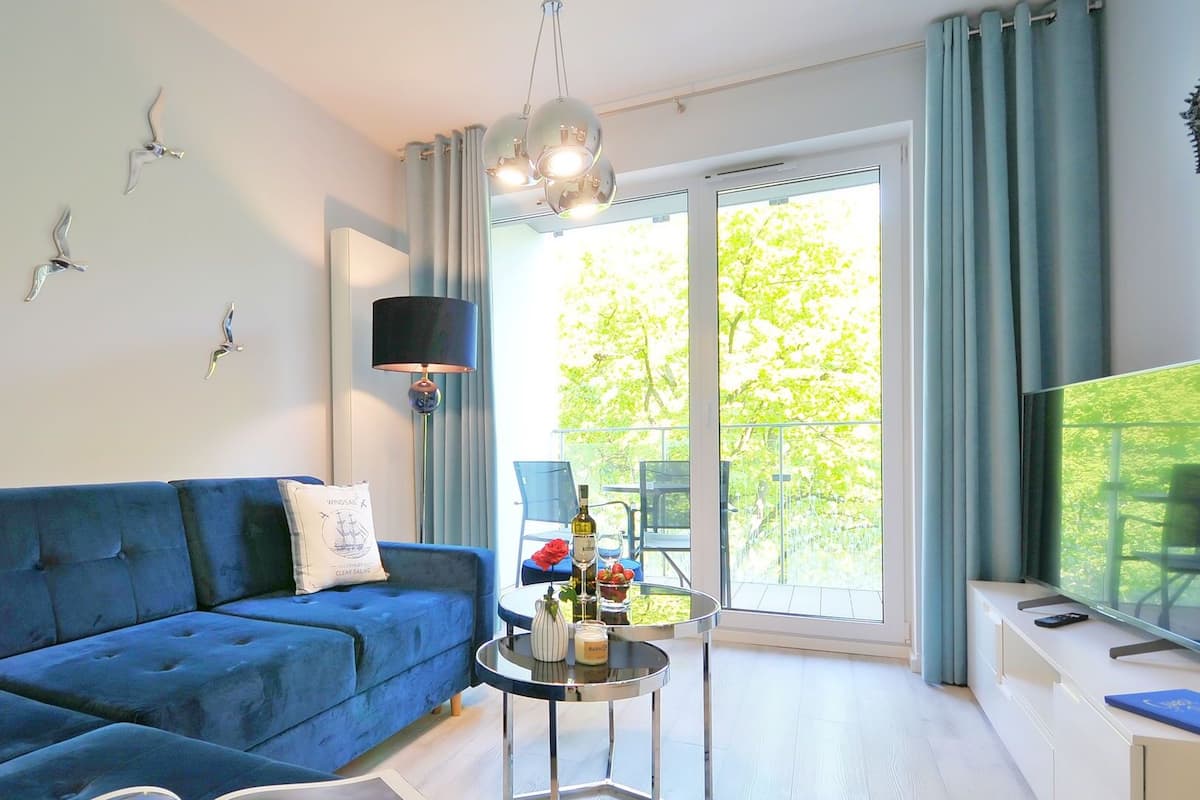 Ein modernes Wohnzimmer mit einem blauen Sofa, einem runden Glastisch und einem Fernseher auf einem weißen Schrank.
