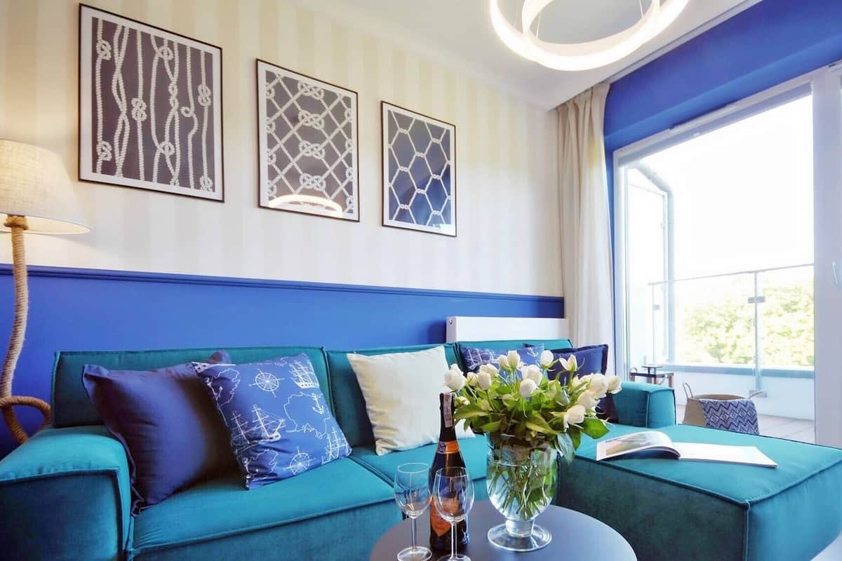 Ein modernes Zimmer mit einem türkisfarbenen Sofa, einem Couchtisch mit Blumenvase und einem Fenster mit Blick ins Freie.