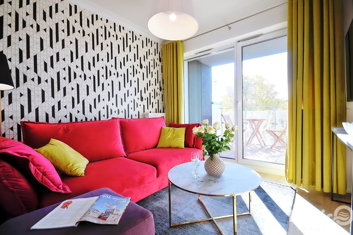 Ein modernes Wohnzimmer mit einem roten Sofa, gelben Kissen, einer weißen Vase mit Blumen und einem runden Couchtisch.