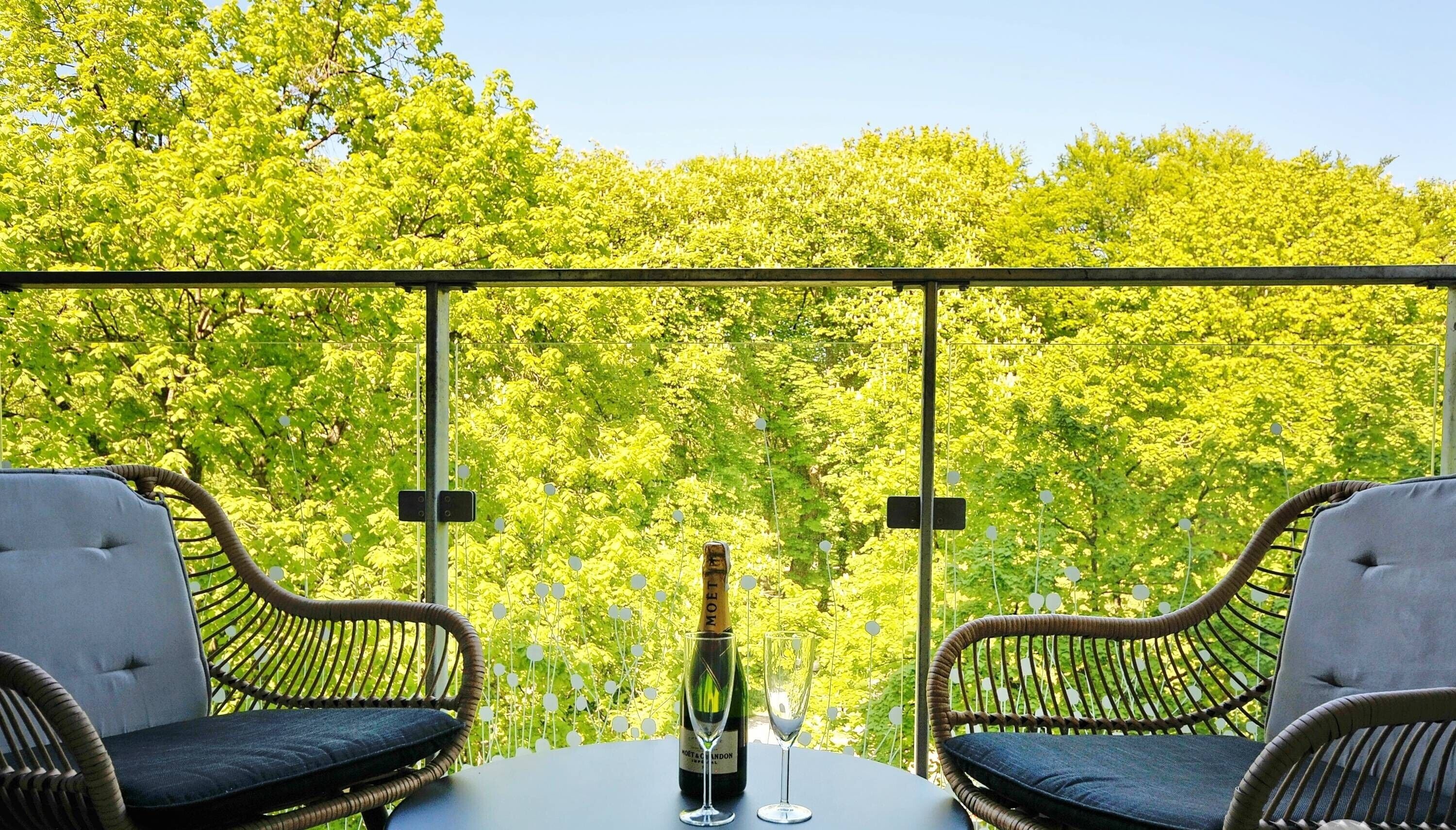 Ein Balkon mit Korbstühlen, einem Tisch, einer Weinflasche und einem Glas.