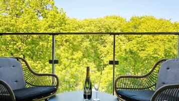 Ein Balkon mit Korbstühlen, einem Tisch, einer Weinflasche und einem Glas.