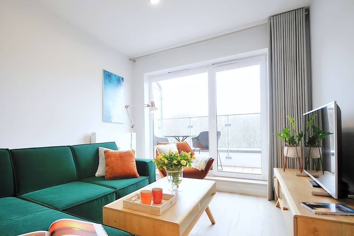 Ein modernes Wohnzimmer mit einem grünen Sofa, einem Holztisch und einem Fernseher.