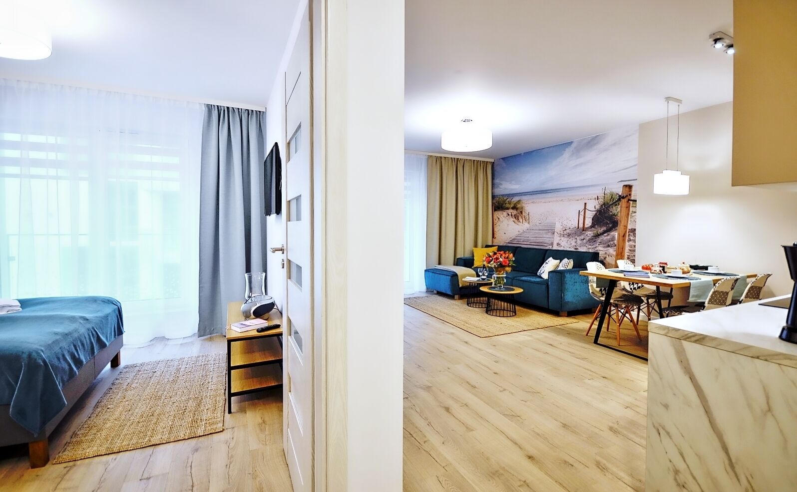 A hotel room with a bed, a desk with a lamp, a sofa, and a dining area with a table and chairs.