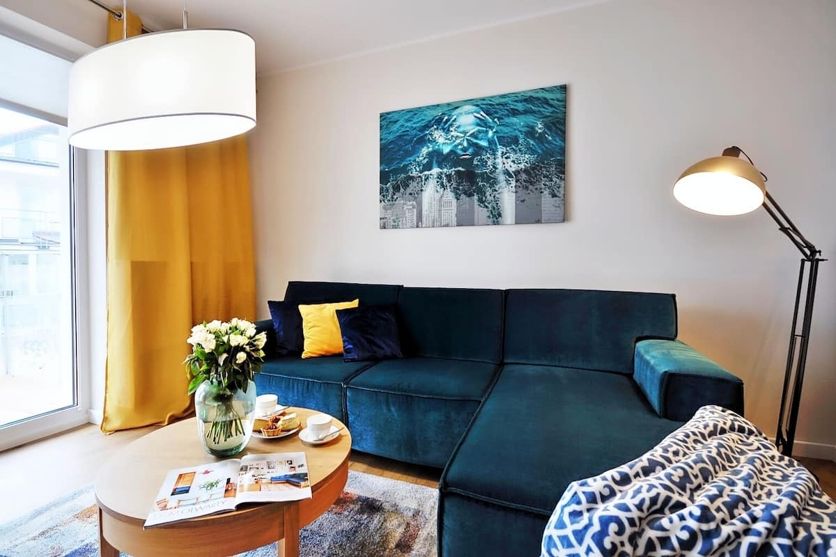 Ein modernes Wohnzimmer mit einem dunkelblauen Sofa, einem runden Couchtisch mit einer Zeitschrift, einem Blumenstrauß und einem Gemälde an der Wand.
